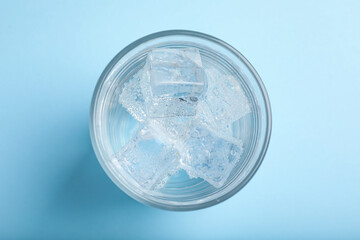 Glass of soda water with ice on light blue background, top view