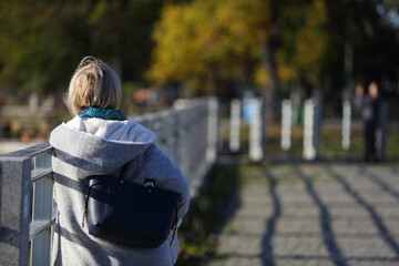 Kobieta z torebką stoi przy bariercew parku.