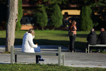Kobieta siedzi na ławce w parku, odpoczynek, relaks. - obrazy, fototapety, plakaty