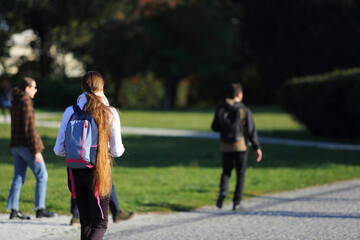 Kobieta z plecakiem i z długimi, pięknymi włosami spaceruje w parku we Wrocławiu.