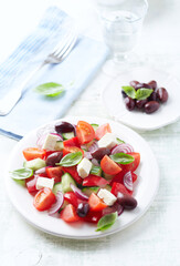 Simple salad with cherry tomatoes, feta cheese, kalamata olives, red pepper and fresh herbs. Bright wooden background.	