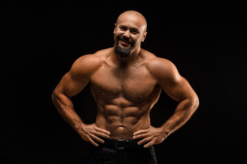 Fototapeta premium Brutal bald man with a beard stands and smiles - photo on a black background.