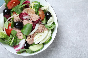 Bowl of delicious salad with canned tuna and vegetables on light grey table, top view. Space for text