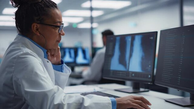 Hospital Laboratory: Black Female Medical Doctor is Working on Computer Analysing Chest, Bones X-rays on Screen. Professional African American Physician Doing Health Care Treatment Research