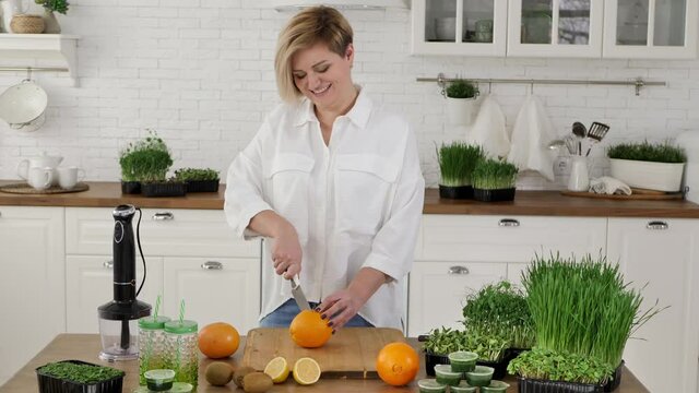 Young woman cuts an orange to make a smoothie