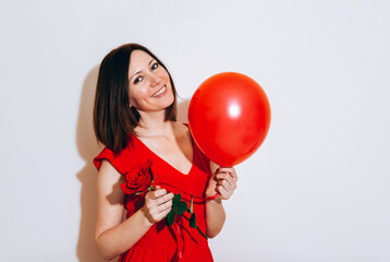 Valentine's Day. Portrait of a beautiful young woman in red dress holding red balloon and red roses on white background. Be my Valentine