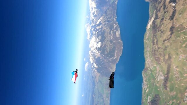 Wingsuit fliers in flight above a mountain lake