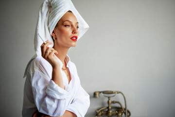 Portrait of beautiful young woman with turban towel on head standing at grey wall