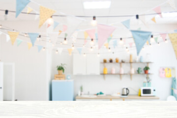 Wooden table top on blurred background of kitchen room. Multicolored flags and a garland of light bulbs..