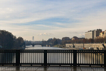 Fototapeta premium View from Vittorio Emanuele I Bridge over the Po River with Umberto I Bridge and the silhouette of the Piedmont Region skyscraper in the foggy background in winter, Turin, Piedmont, Italy