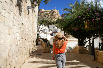 Exploring Alicante in Spain. Young traveler woman walking in the neighborhood Santa Cruz looking at Mount Benacantil with Santa Barbara castle in Alicante, Spain. - obrazy, fototapety, plakaty