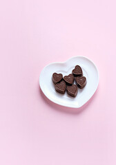 chocolate heart candies on white plate, abstract pink background. sweets gift for Valentine's day. 14 february holiday. candy heart, symbol of love, romance. minimal style design. top view. copy space