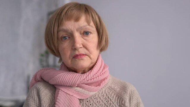 Portrait of senior lady. Close-up indoor portrait of sad old woman with short hair and pink scarf. Stylish mature woman alone