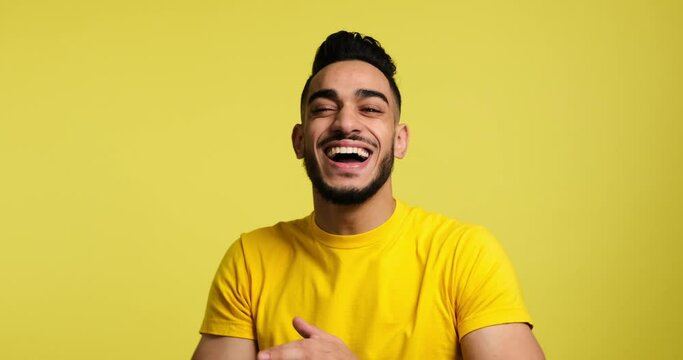Portrait of cheerful young man laughing and clapping hand over yellow background