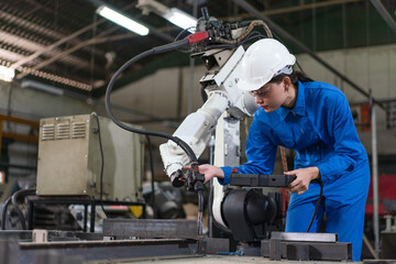 Fototapeta na wymiar Female automation engineer wear a blue uniform with helmet safety inspection control a robot arm welding machine with a remote system in an industrial factory. Artificial intelligence concept.