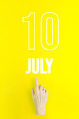 July 10th. Day 10 of month, Calendar date.Hand finger pointing at a calendar date on yellow background.Summer month, day of the year concept.