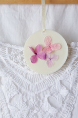 Scented sachet with flowers hanging near stylish clothes, closeup view