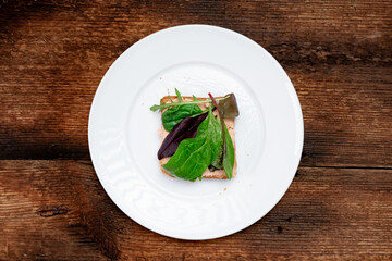 Vegetarian sandwich. Toast with a creamy spread and assorted edible salad leaves. White plate, dark wooden background. Healthy eating. Food concept.