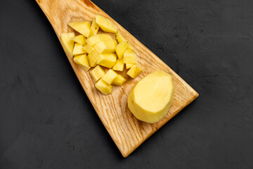 Sliced raw potatoes on a cutting wooden board. dark background. Preparation for cooking. Food background. Recipe.