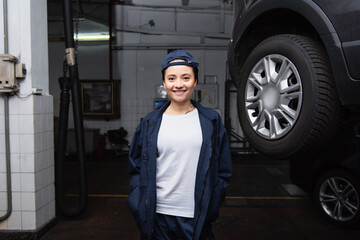 Smiling mechanic looking at camera near car in garage.
