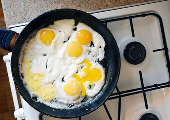 Fried eggs in a frying pan on a gas stove, top view