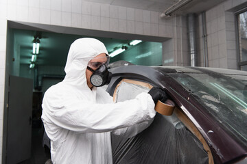 Workwoman in respirator and goggles applying tape on cellophane while working in car service.