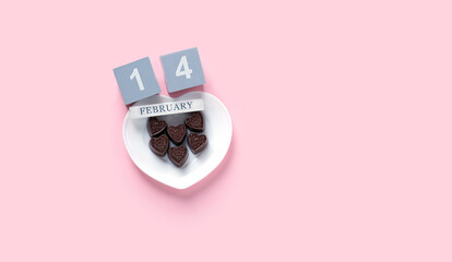chocolate heart candies on white plate, 14 february date calendar on pink background. sweets gift for Valentine's day. candy heart, symbol of love, romance. minimal style design. flat lay. copy space