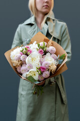 A woman holds a bouquet of peonies against a gray background. Pastel colors. Spring tones.