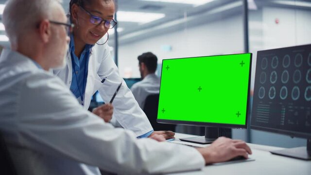 Medical Hospital: Neurologist and Neurosurgeon Talk, Use Green Screen Chroma Key Computer, Analyse Patient MRI Scan. Brain Health Research Clinic: Two Smiling Physicians Look at CT Scan find Treatment