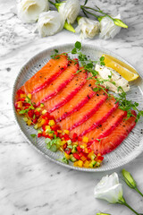 Lightly salted salmon, colored with beetroot juice with finely chopped fresh vegetables in a festive plate on a marble background. Restaurant banquet menu.