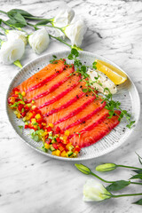 Lightly salted salmon, colored with beetroot juice with finely chopped fresh vegetables in a festive plate on a marble background. Restaurant banquet menu.