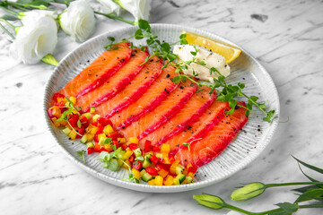 Lightly salted salmon, colored with beetroot juice with finely chopped fresh vegetables in a festive plate on a marble background. Restaurant banquet menu.
