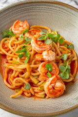 Spaghetti with shrimps in tomato sauce with green onions in a festive plate on a marble background. Restaurant banquet menu.