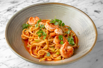 Spaghetti with shrimps in tomato sauce with green onions in a festive plate on a marble background. Restaurant banquet menu.