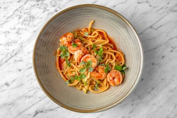 Spaghetti with shrimps in tomato sauce with green onions in a festive plate on a marble background. Restaurant banquet menu.
