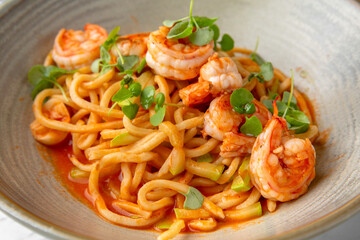 Spaghetti with shrimps in tomato sauce with green onions in a festive plate on a marble background. Restaurant banquet menu.
