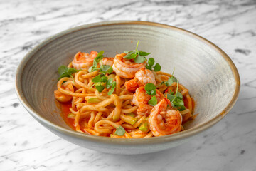 Spaghetti with shrimps in tomato sauce with green onions in a festive plate on a marble background. Restaurant banquet menu.