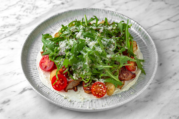 Salad with homemade fried potato, grilled mushrooms, fresh vegetables and arugula in a festive plate on a marble background. Restaurant banquet menu.