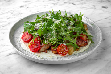 Salad with homemade fried potato, grilled mushrooms, fresh vegetables and arugula in a festive plate on a marble background. Restaurant banquet menu.