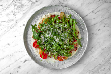 Salad with homemade fried potato, grilled mushrooms, fresh vegetables and arugula in a festive plate on a marble background. Restaurant banquet menu.