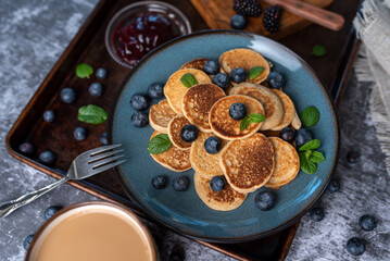 Mini pancakes on a plate with blueberries, jelly and butter. Protein pancakes for smaller bites. Diet and healthy living breakfast option. Dutch mini pancakes. 
