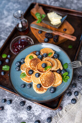 Mini pancakes on a plate with blueberries, jelly and butter. Protein pancakes for smaller bites. Diet and healthy living breakfast option. Dutch mini pancakes. 