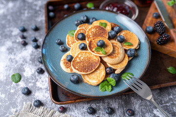 Mini pancakes on a plate with blueberries, jelly and butter. Protein pancakes for smaller bites. Diet and healthy living breakfast option. Dutch mini pancakes. 