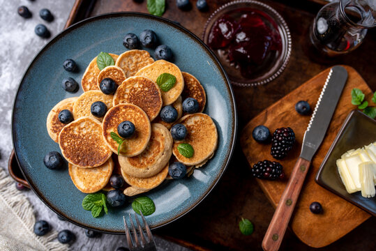 Mini pancakes on a plate with blueberries, jelly and butter. Protein pancakes for smaller bites. Diet and healthy living breakfast option. Dutch mini pancakes. 