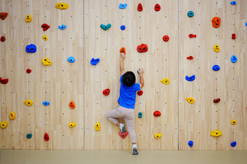 Little boy climbing a rock wall indoor. - obrazy, fototapety, plakaty