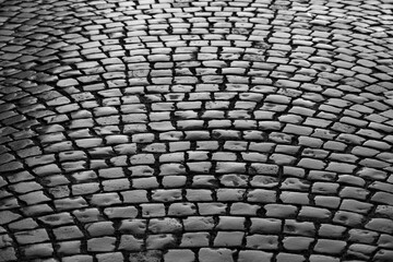 Old cobblestone street in Iserlohn Sauerland Germany. Wet shiny historic basalt ashlars and blocks reflecting sunshine after rain.  Pavement background, black and white greyscale with high contrast.