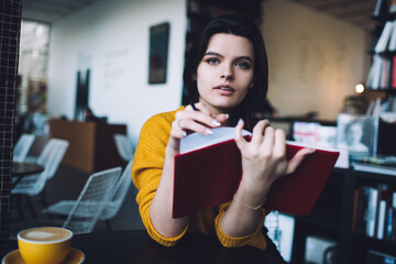 Thoughtful woman flipping notebook pages and looking at camera