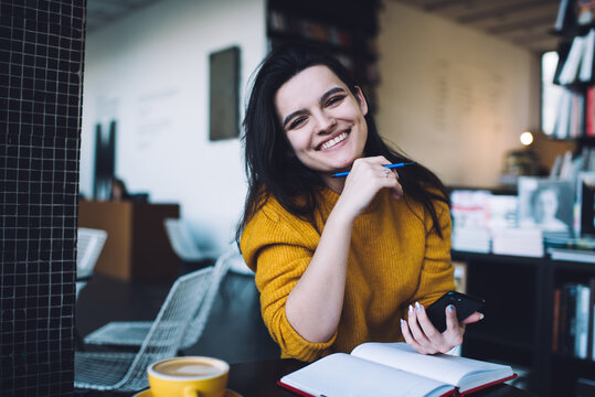 Smiling businesswoman with planner and mobile in cafe