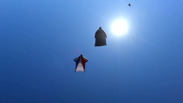 Wingsuit fliers soar in blue sky