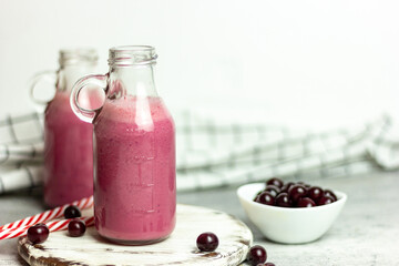 A bottle of cherry smoothies on a white background, cherries in bulk and in a plate. Morning summer breakfast